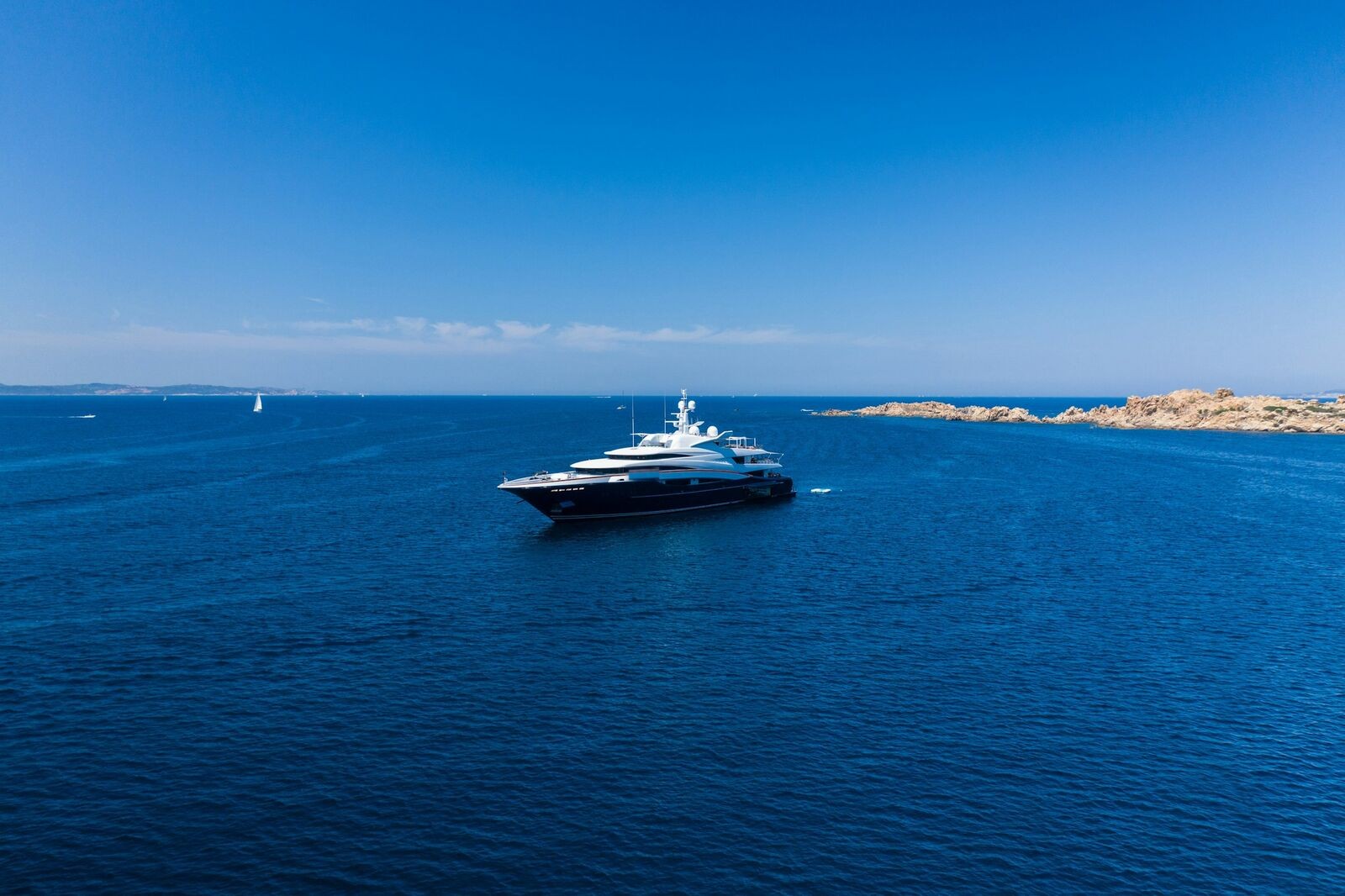 A superyacht at anchor off a rocky coastline