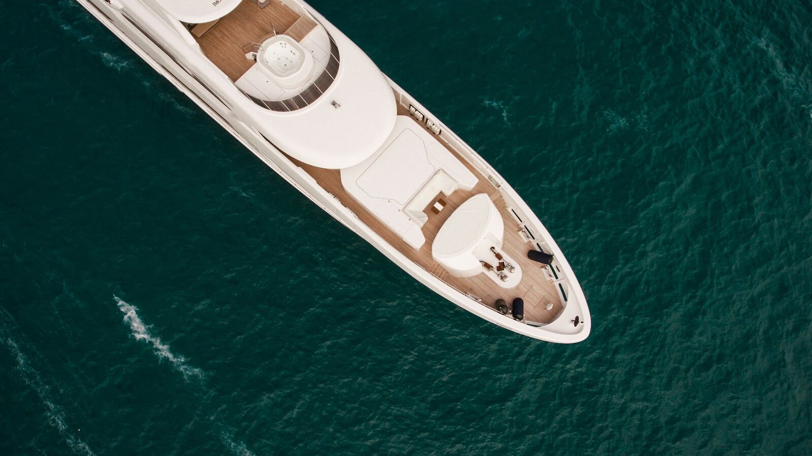 Aerial view of the foredeck of a white yacht on dark green water