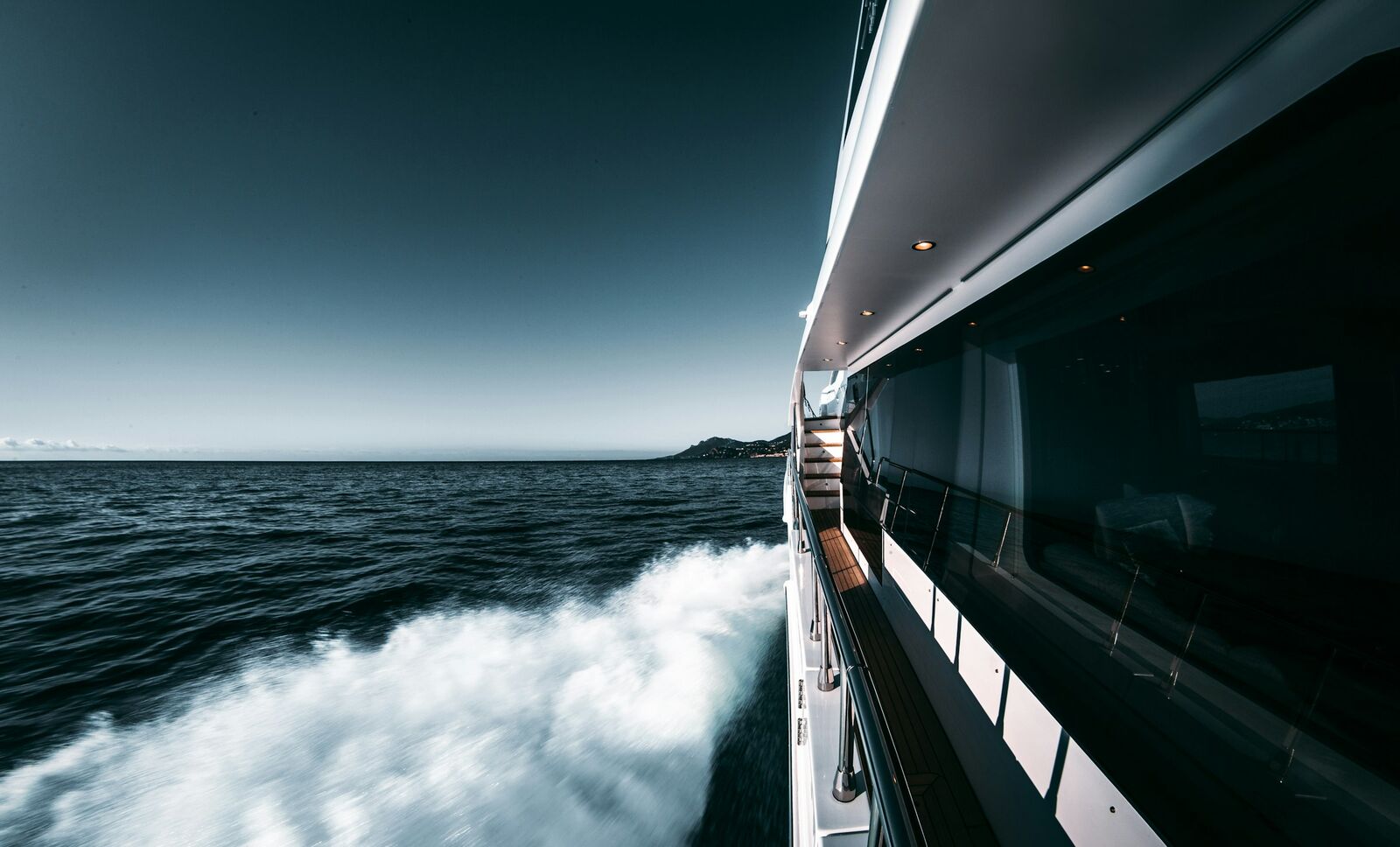 The side deck of a superyacht underway, with white water in her wake